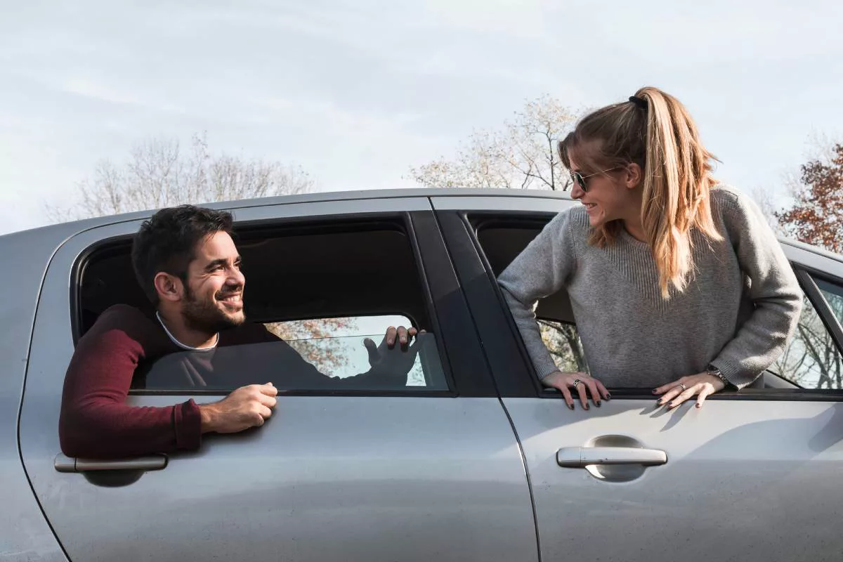 Un homme et une femme souriants, penchés aux vitres d’une voiture grise