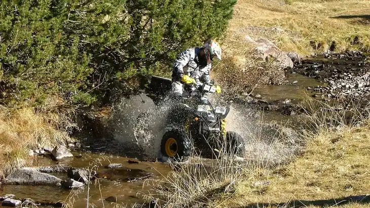 Quad noir traversant un ruisseau, conducteur casqué